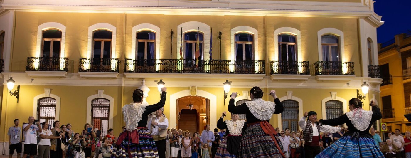 Grupo de danzas tradicionales bailando ante la fachada iluminada del Ayuntamiento de Cheste