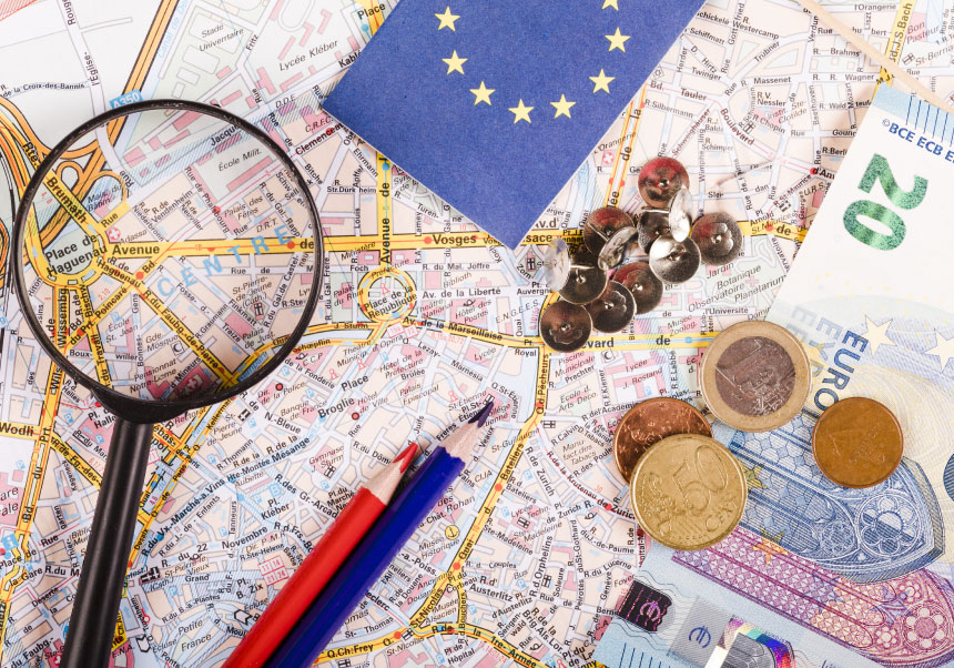 Picture of a map and over it money, pencils and a magnifying glass
