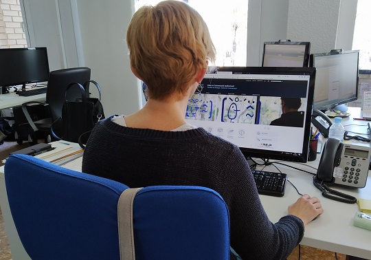 Una empleada ante un ordenador con la web de la Unitat Web i Màrqueting en pantalla.