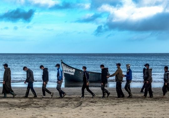 Fotografía de inmigrantes y una patera en la playa.