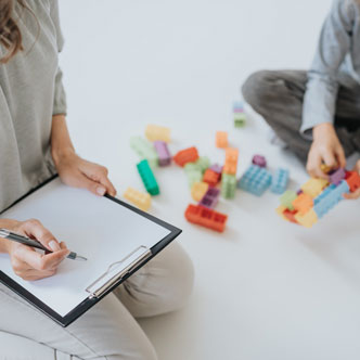 Protocolo TEA - Imagen de una mujer tomando notas mientras observa como un niño juega