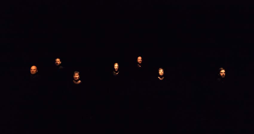 Set actors i actrius sobre fons negre il·luminant-los la cara