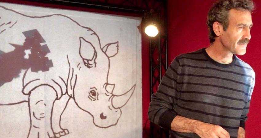 A man in front of a drawing of a rhinoceros