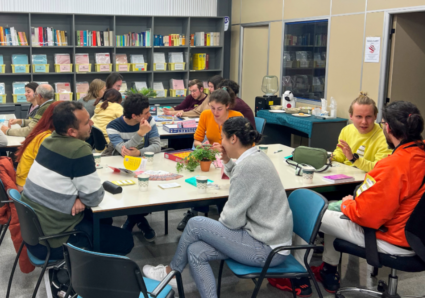 Imagen del evento:Un grupo de personas conversa alrededor de una mesa en un centre d'aprenentatge de llengües.
