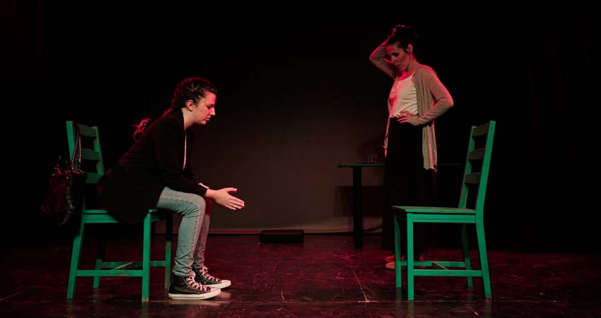 Una dona asseguda i una altra dempeus en l'escenari