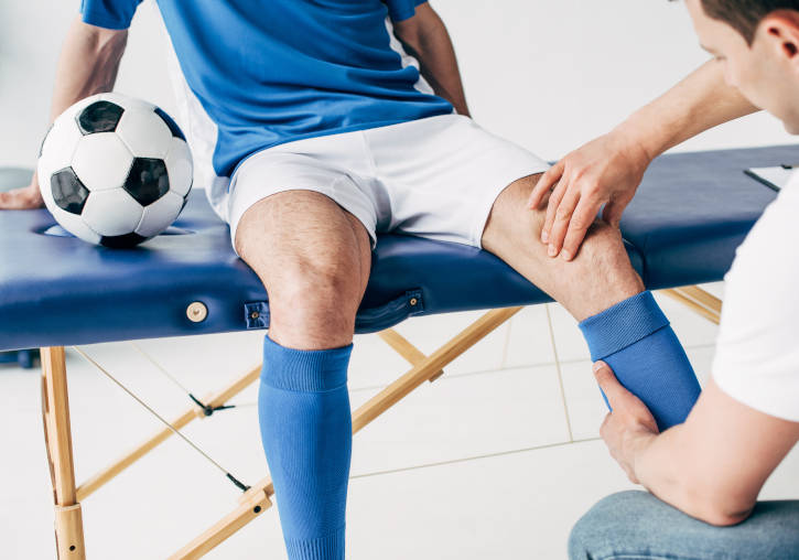 Un fisioterapeuta tracta la cama d'un futbolista.