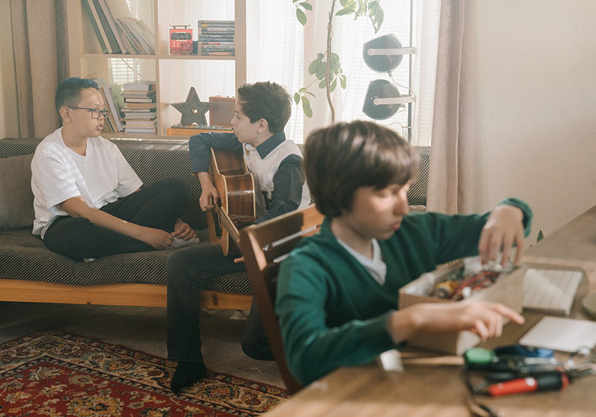 Three kids playing in a living room, one of them playing the guitar
