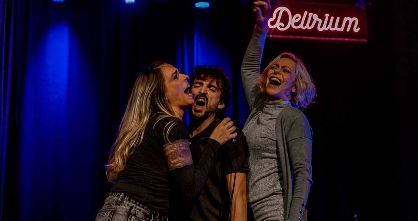 Dos mujeres y un hombre bebiendo y gritando