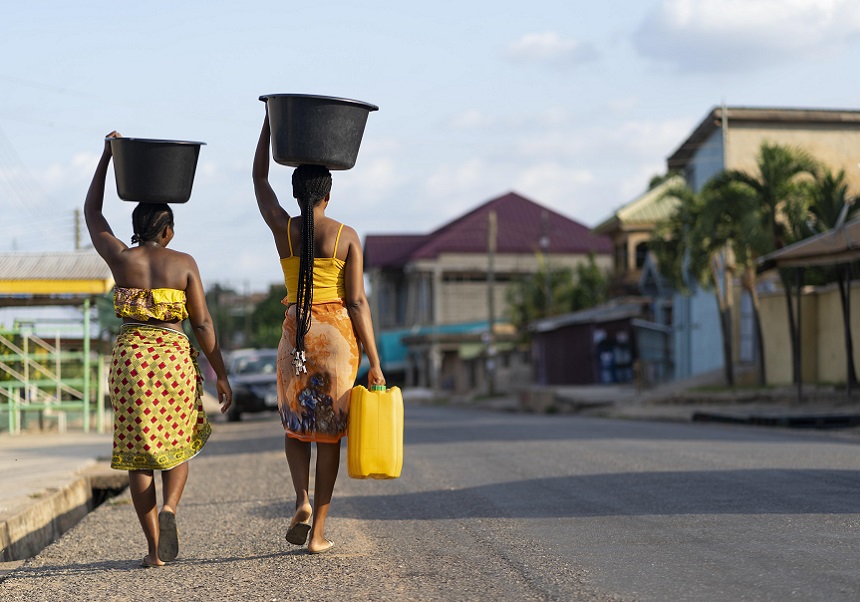 Dos mujeres guineanas cargan sobre sus cabezas cubos de agua.