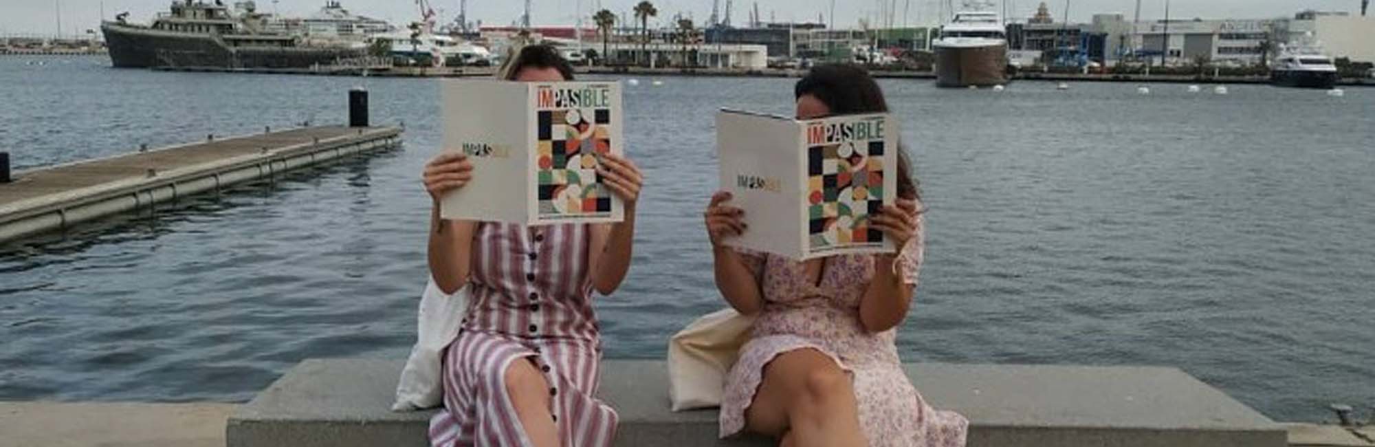 Dos mujeres sentadas leyendo una revista. 
