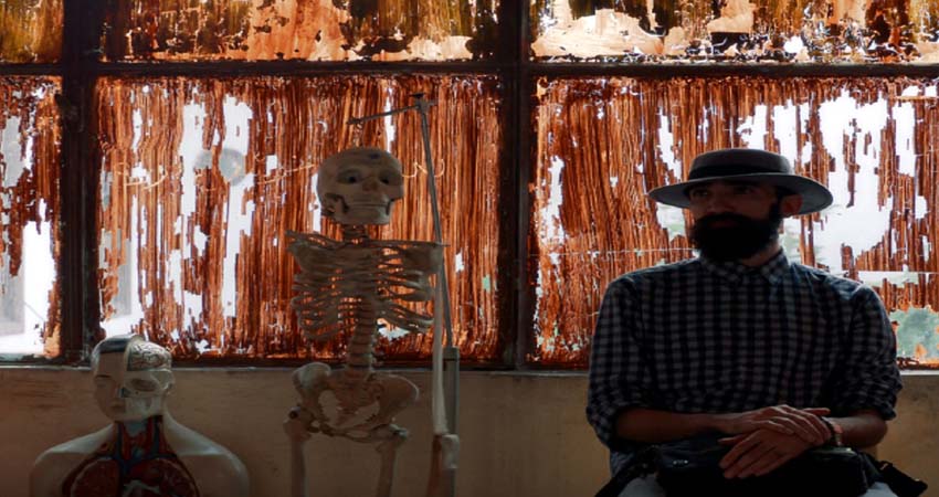 Fotograma. Un hombre sentado junto a un esqueleto