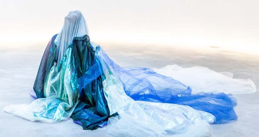 A woman, completely covered, sitting on the ground looking up at the sky