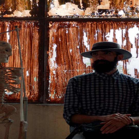 Fotograma. Un hombre sentado junto a un esqueleto