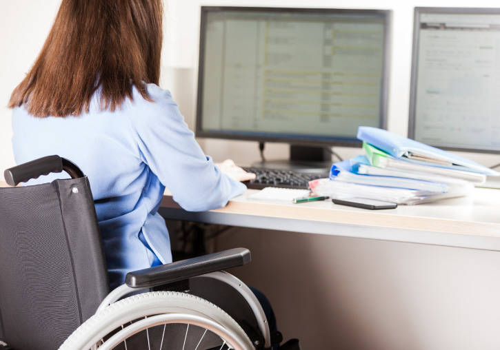 Una dona en cadira de rodes treballa davant d'un ordinador.