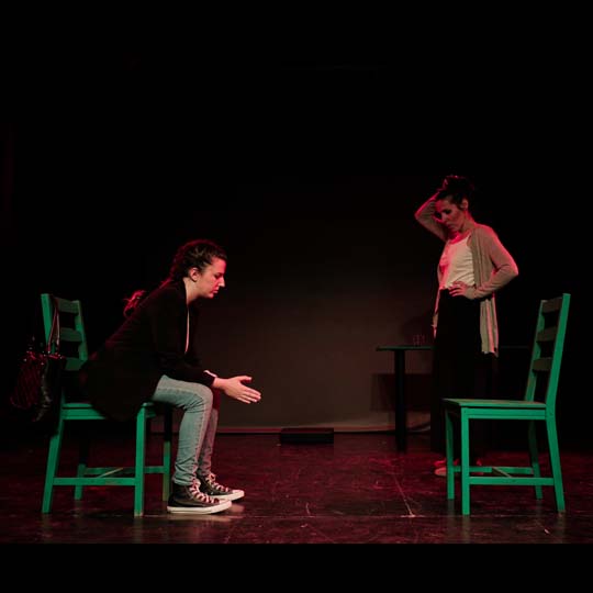 A woman sitting and another standing on stage