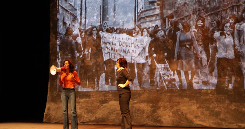 Dos dones a l’escenari i darrere, projecció d’una manifestació