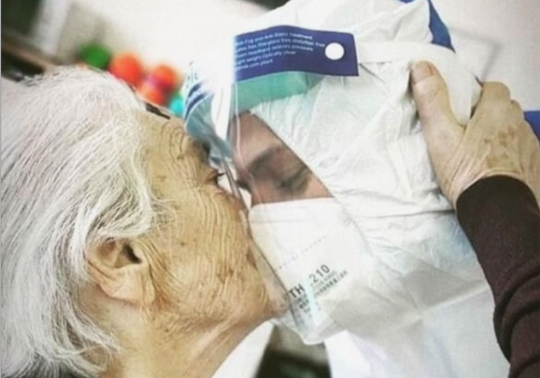 Fotografia d'una anciana besant a un treballador sanitari amb vestit i màscara anticontagi.