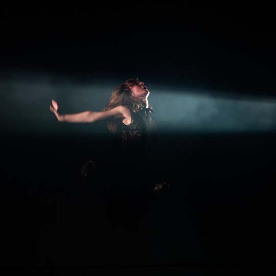 Una mujer iluminada por un foco actuando