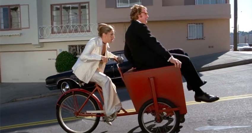 Una dona amb bicicleta portant davant en un calaix a un home
