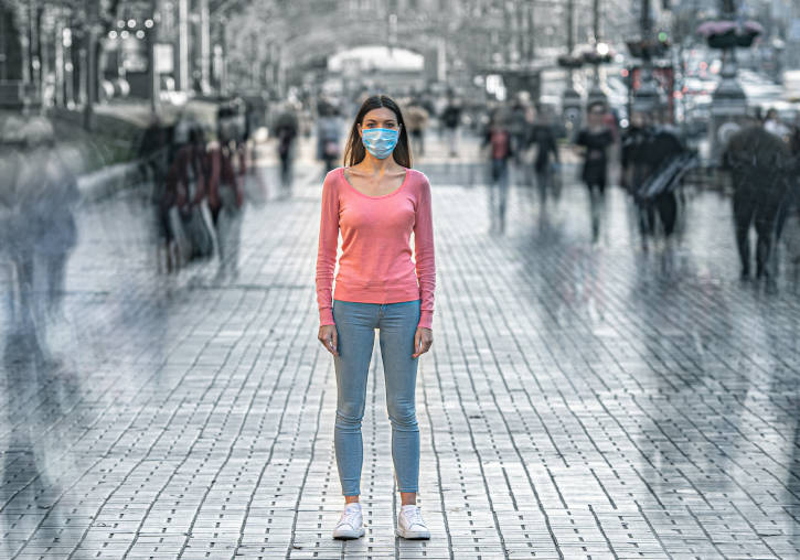 Una mujer con mascarilla, parada de pie en medio de la calle.