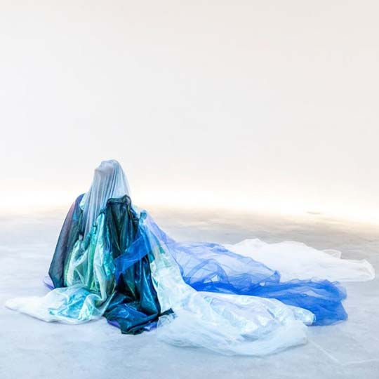 A woman, completely covered, sitting on the ground looking up at the sky