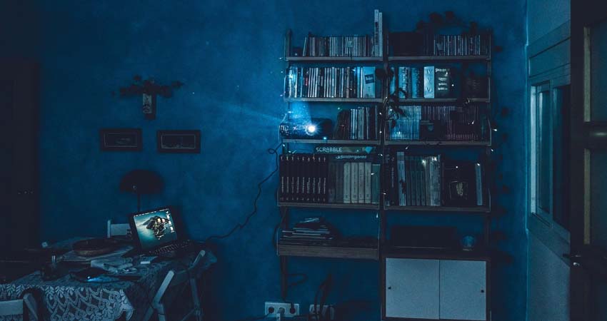 Foto de una estancia de tono azul con librería y un proyector