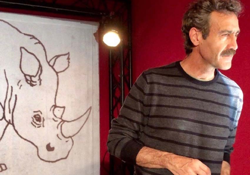 A man in front of a drawing of a rhinoceros