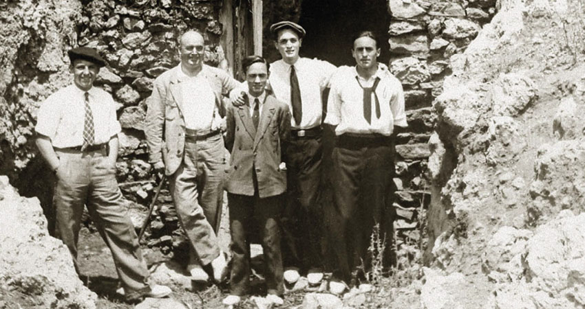 Cinco hombres delante de la puerta de una construcción derruida