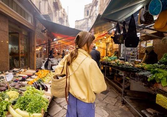 Persona comprando alimentos frescos en un mercado tradicional con puestos de frutas y verduras.