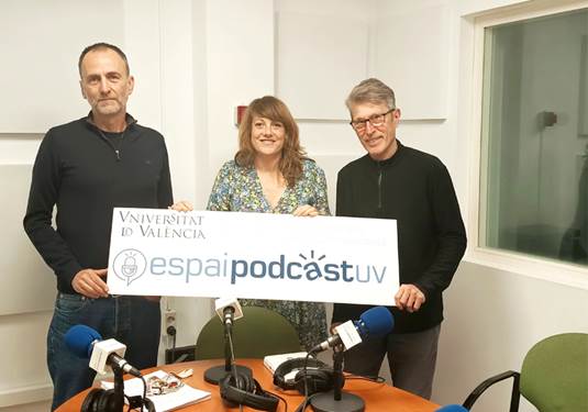 Tres personas en un estudio de radio de EspaiP�dcastUV con micr�fonos y un cartel del p�dcast.
